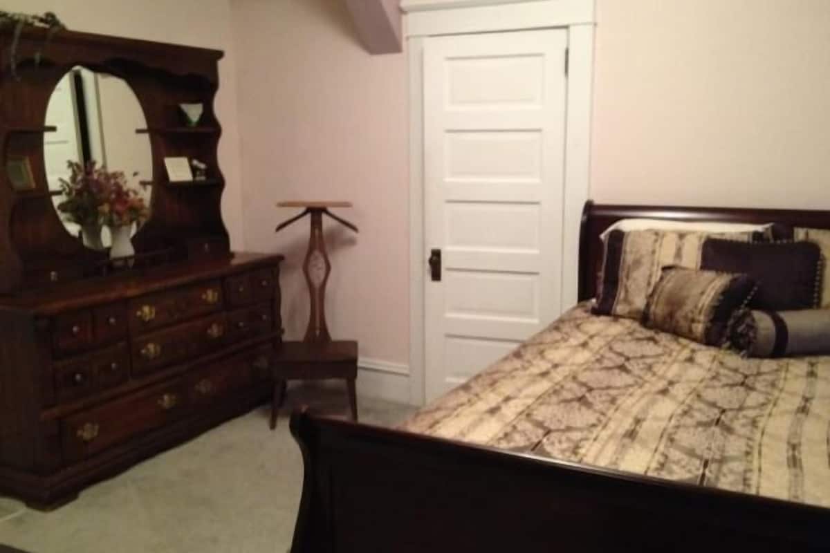 A bedroom with a wooden dresser, a bed with patterned bedding, and a white door.