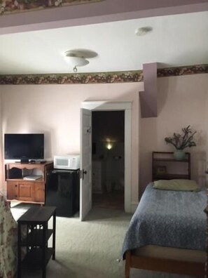 A bedroom with a bed, a television, a desk, and a door leading to a bathroom. - Victorian Charm Inn (Towanda)