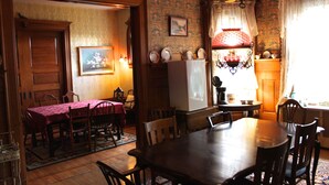 A dining area with a wooden table and chairs, a refrigerator, and a patterned wallpaper. - Victorian Charm Inn (Towanda)