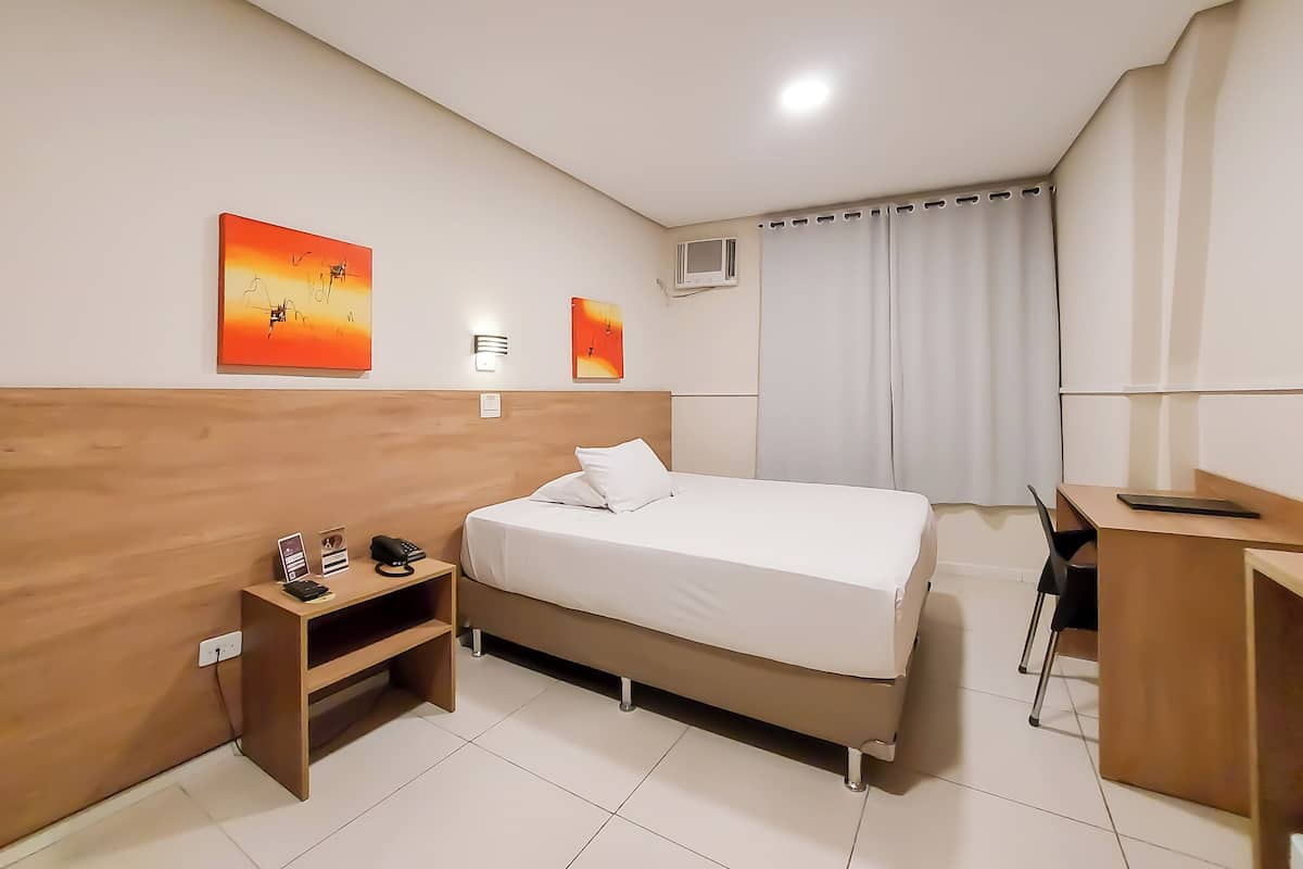 A hotel room with a bed, bedside table, desk, and two wall-mounted artworks.