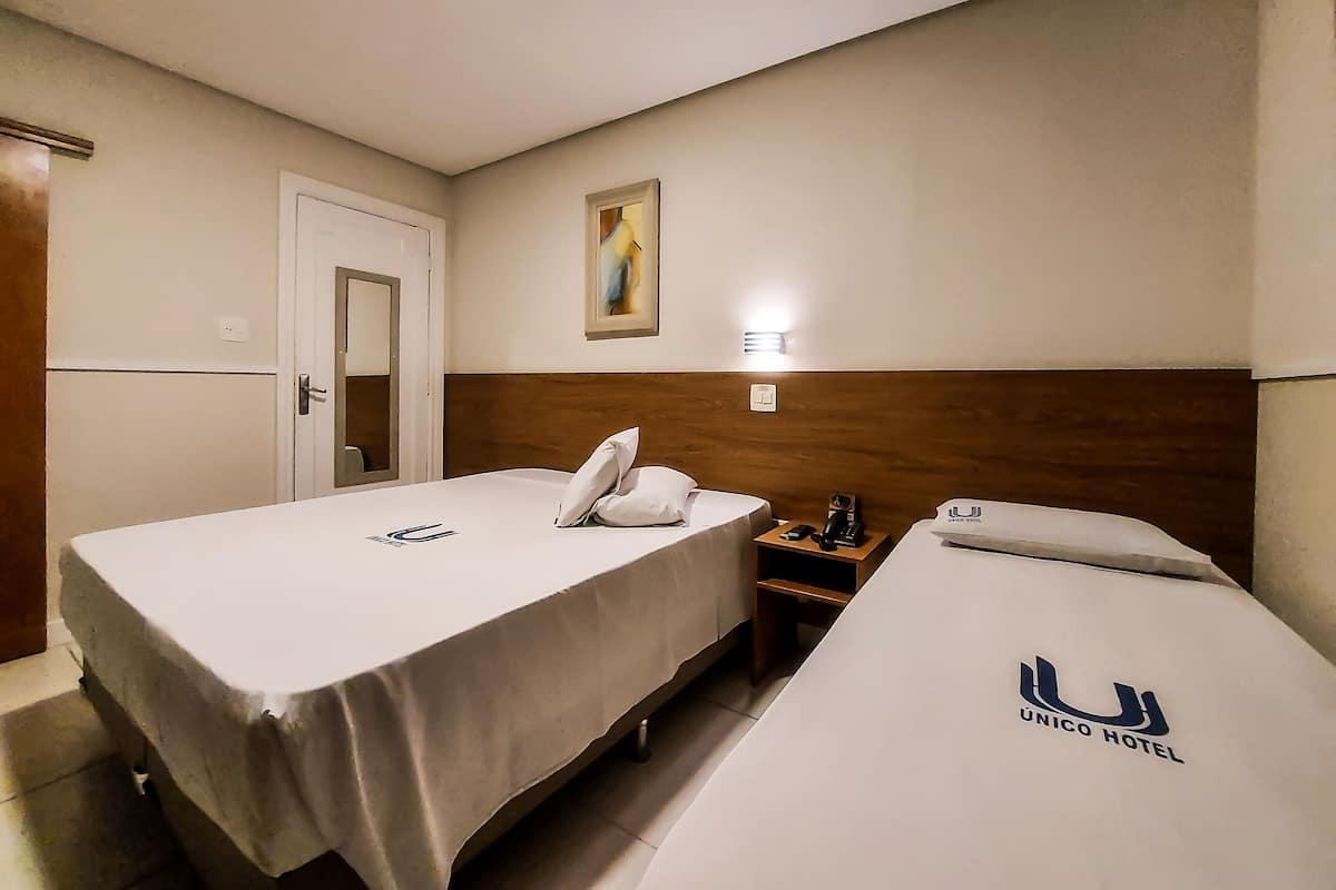 A hotel room with two beds, a wooden headboard, a nightstand with a phone and a lamp, and a painting on the wall.