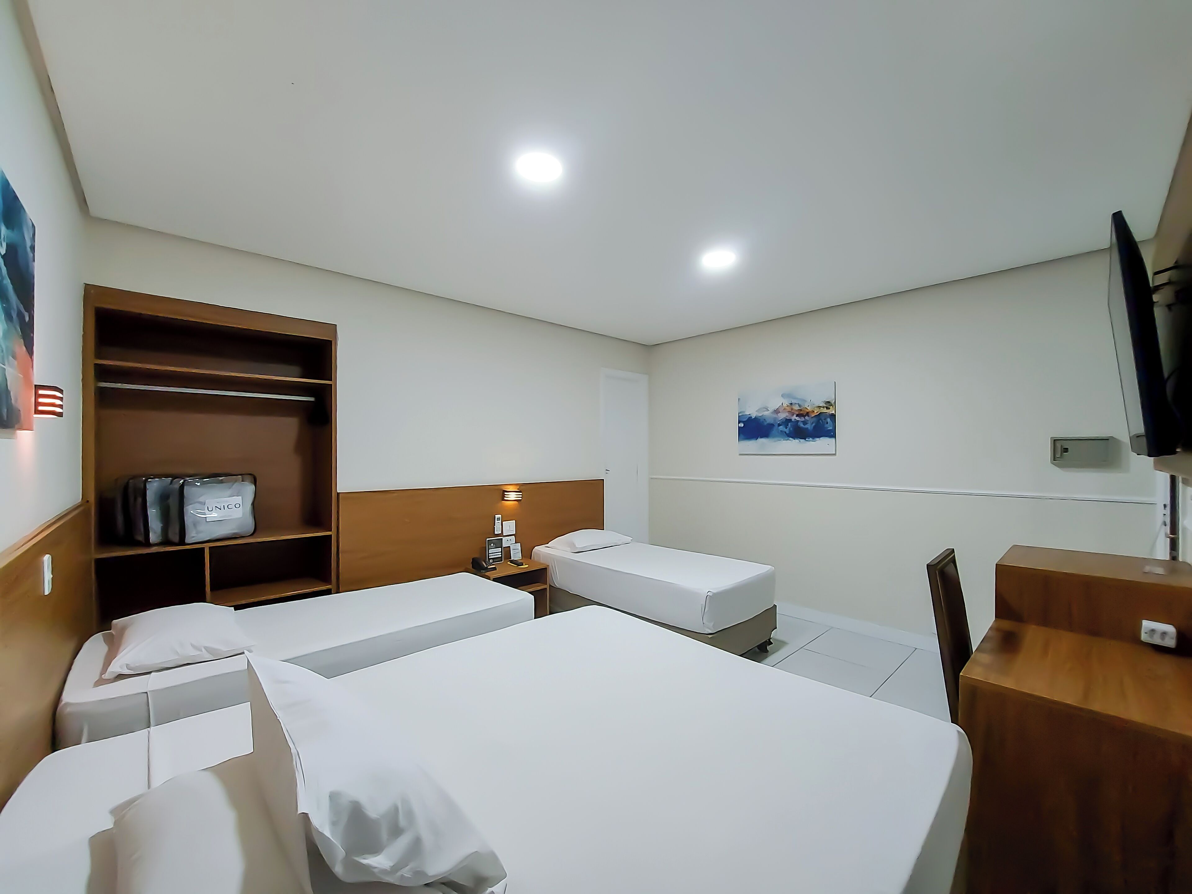 A hotel room with two beds, a wardrobe, a desk, and a TV.