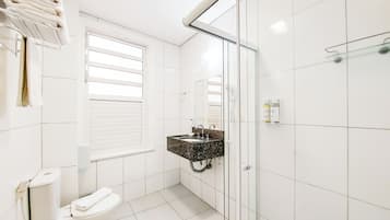 A modern bathroom with white tiles, a glass shower enclosure, a toilet, and a vanity with a marble countertop.