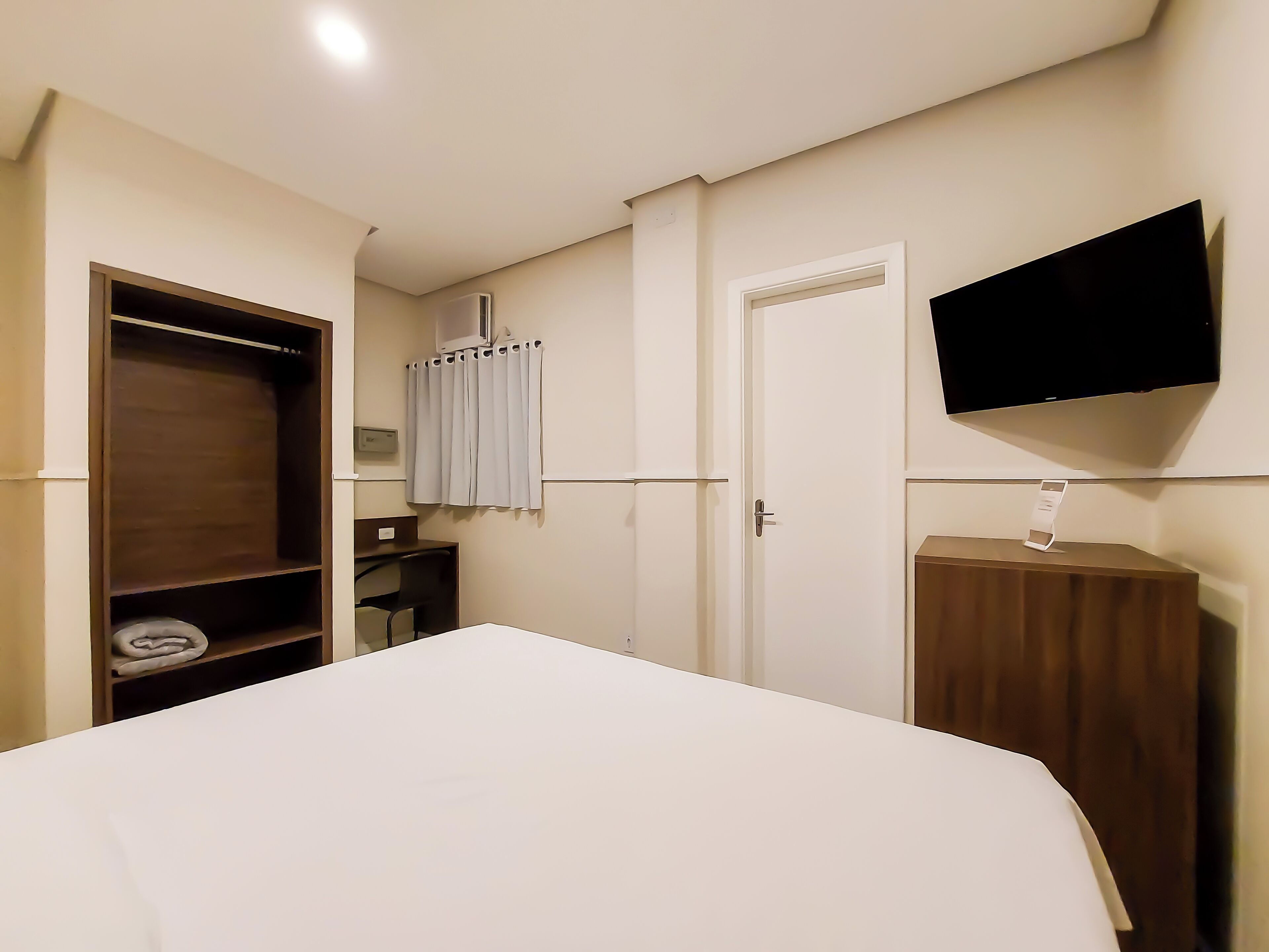 Un dormitorio con cama, armario, escritorio, silla, televisor y cortina.
