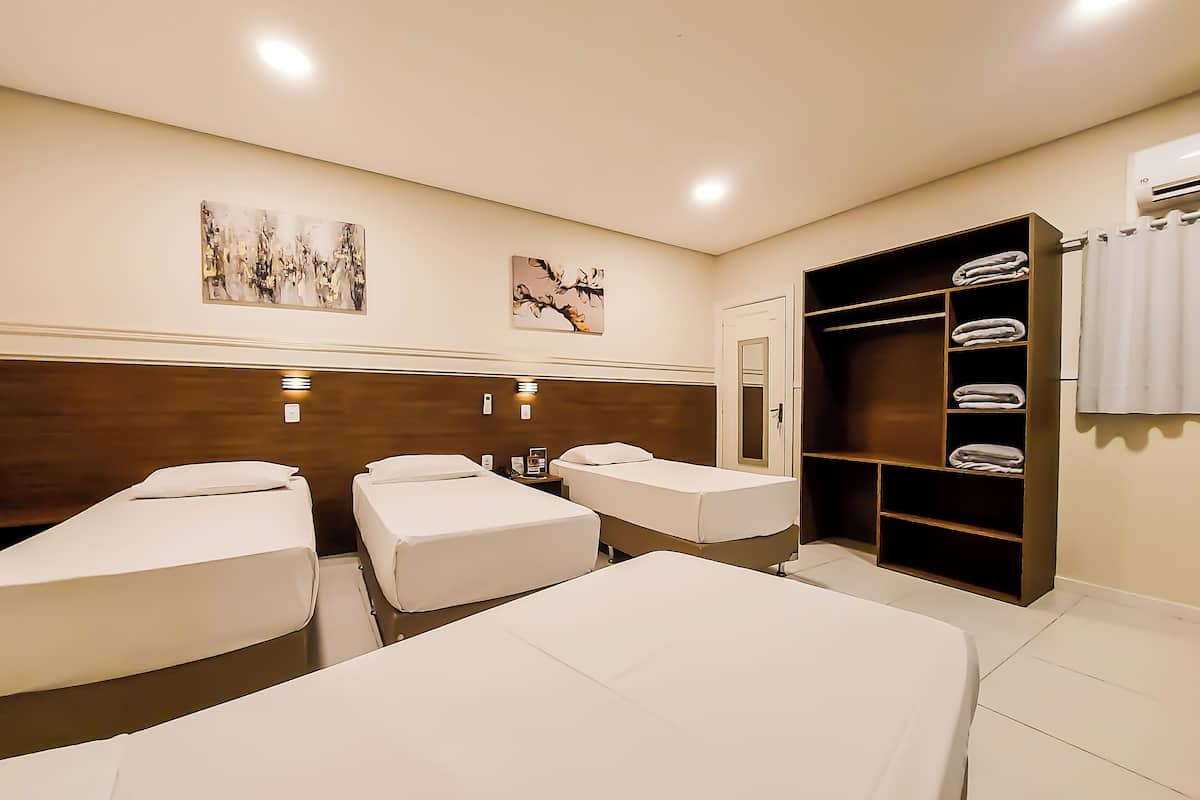A hotel room with three beds, a wardrobe, and artwork on the walls.