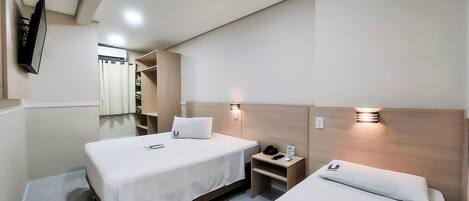 A hotel room with two beds, a nightstand, a mirror, and a TV mounted on the wall.