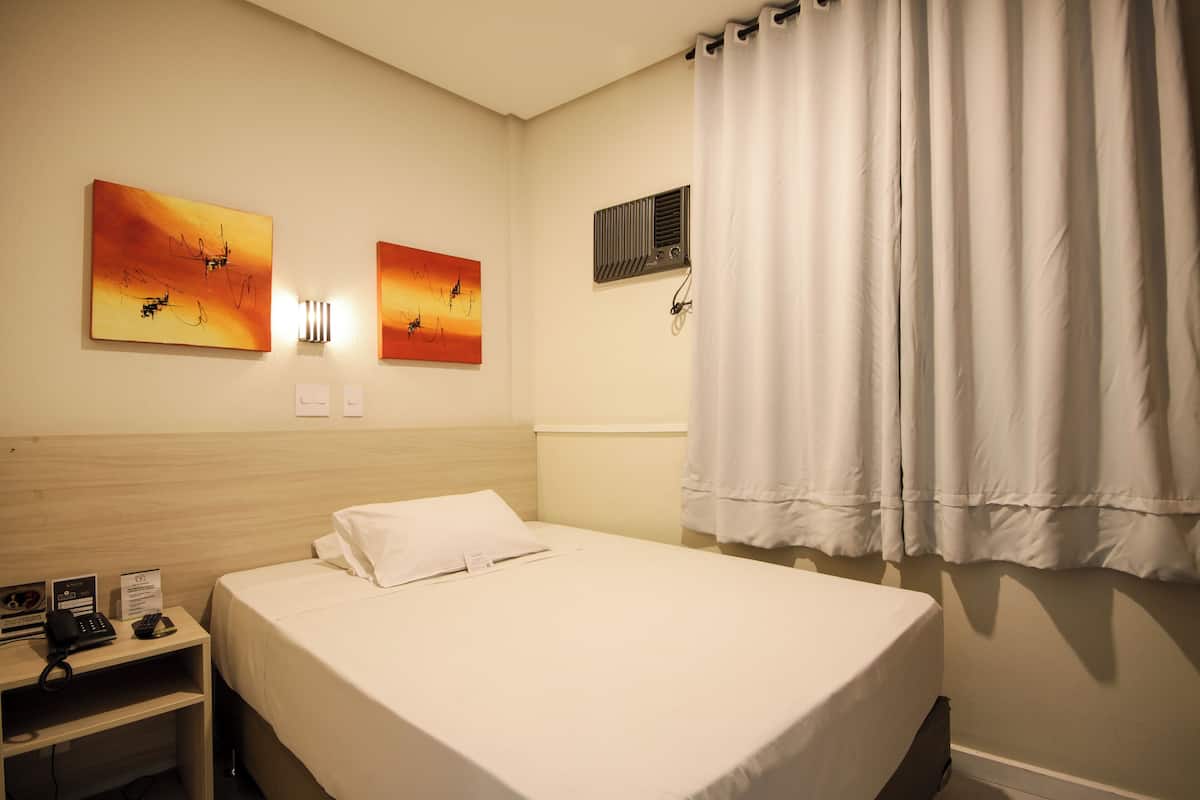 A hotel room with a bed, a nightstand, a telephone, and two wall-mounted paintings.