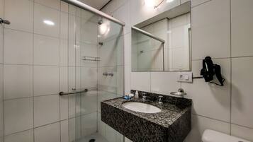 A modern bathroom with a glass shower enclosure, a granite countertop sink, and a wall-mounted mirror.