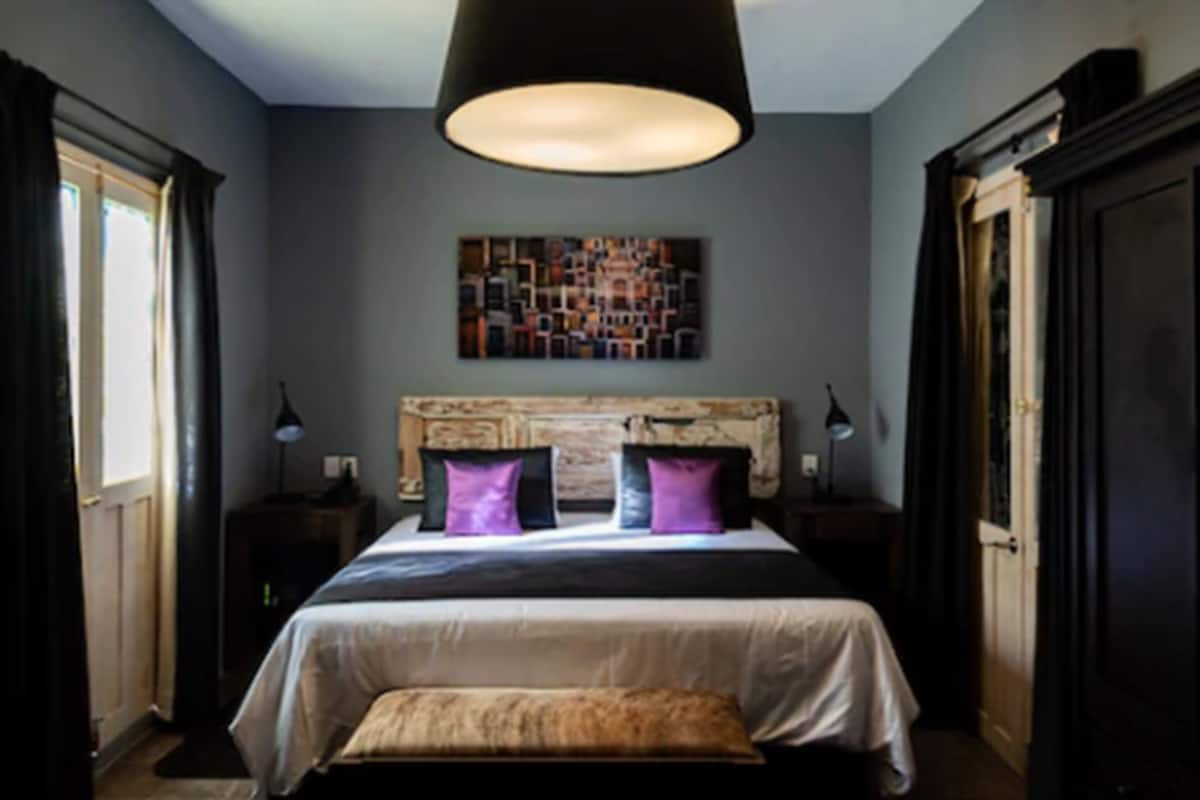 A bedroom with a large bed, a headboard, a wall-mounted artwork, and a pendant light.