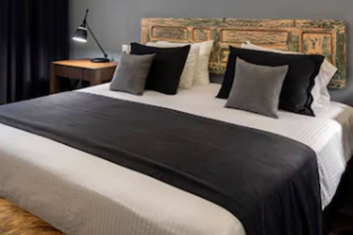 A hotel room with a large bed, a nightstand, a lamp, a headboard with a decorative panel, and a framed artwork on the wall.