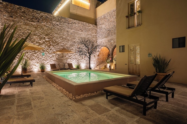 Zona de piscina al aire libre con paredes de piedra, sillas de descanso y sombrillas.