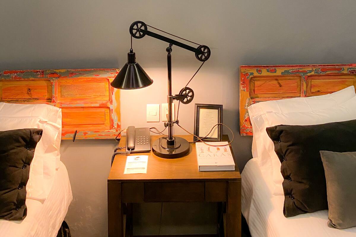 A hotel room with two beds, a desk with a lamp, a telephone, and a framed picture on the wall.