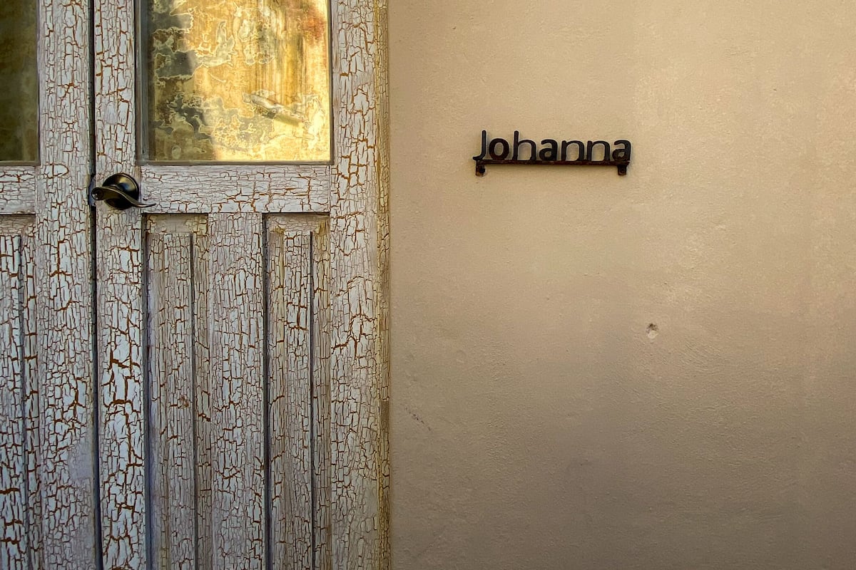 A weathered wooden door with a textured glass panel and a nameplate reading "Johanna" on a plain wall.