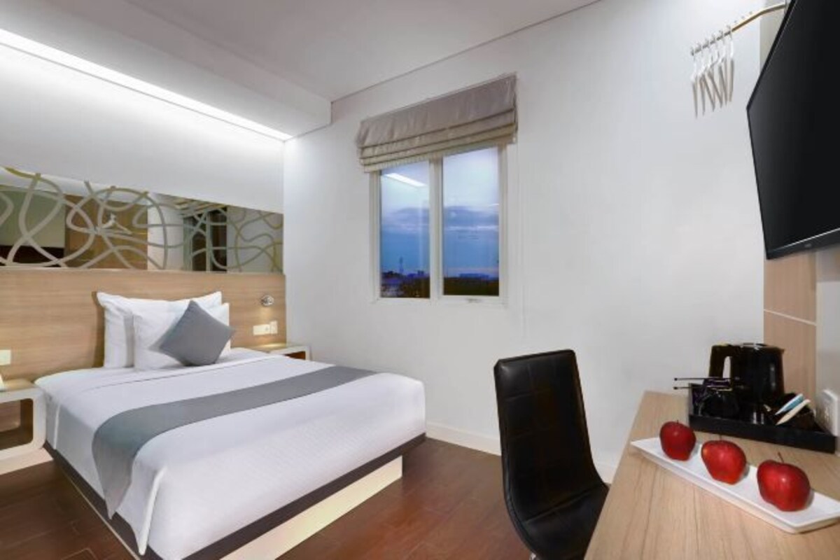 Una camera d'albergo con un letto, una scrivania con una sedia, una televisione e una finestra vista.