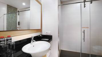 Un baño moderno con un lavamanos blanco, encimera negra y cabina de ducha con paredes de vidrio.
