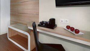 Ein modernes Hotelzimmer mit einer Wandpaneele aus Holz, einem Flachbildfernseher, einem Schreibtisch mit Kaffeemaschine und einer Schale Äpfel.
