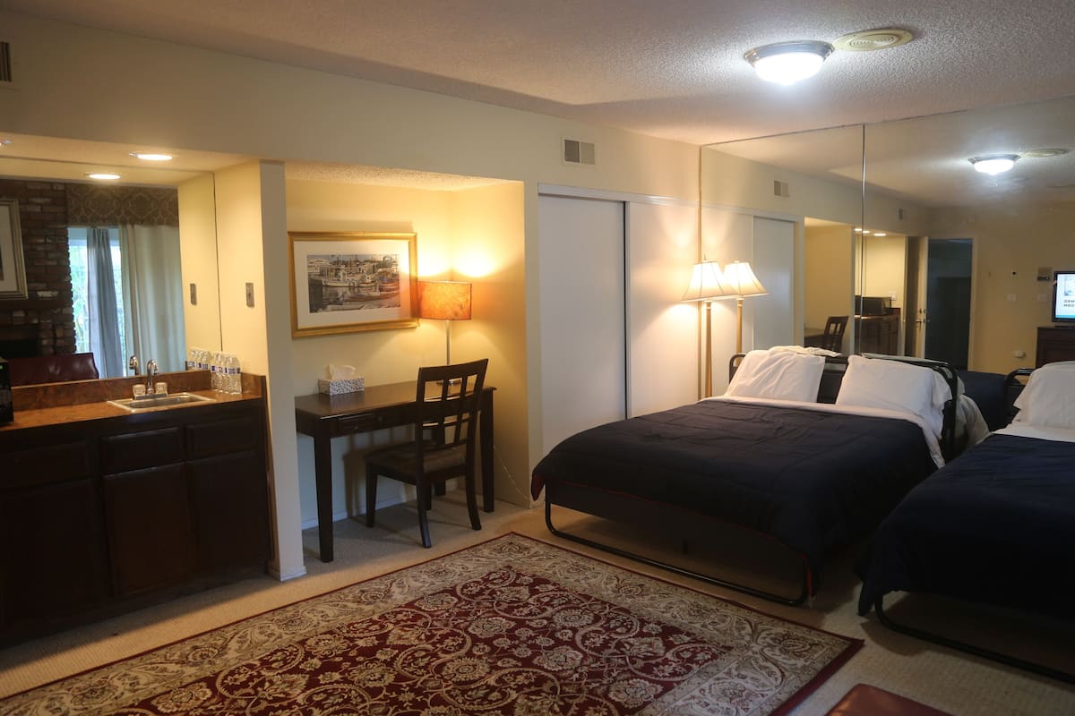 A hotel room with a bed, a desk, a chair, a mirror, and a rug.