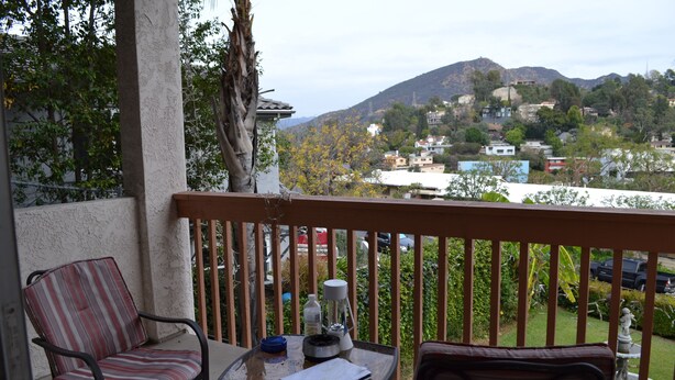 A balcony with two chairs, a table, and a view of a hillside town. - Bed and Breakfast in Hollywood Hills (Los Angeles)