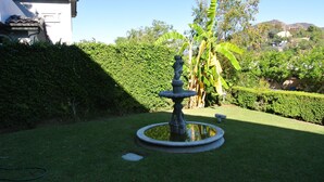 A well-maintained garden with a stone fountain, neatly trimmed hedges, and a banana tree. - Bed and Breakfast in Hollywood Hills (Los Angeles)