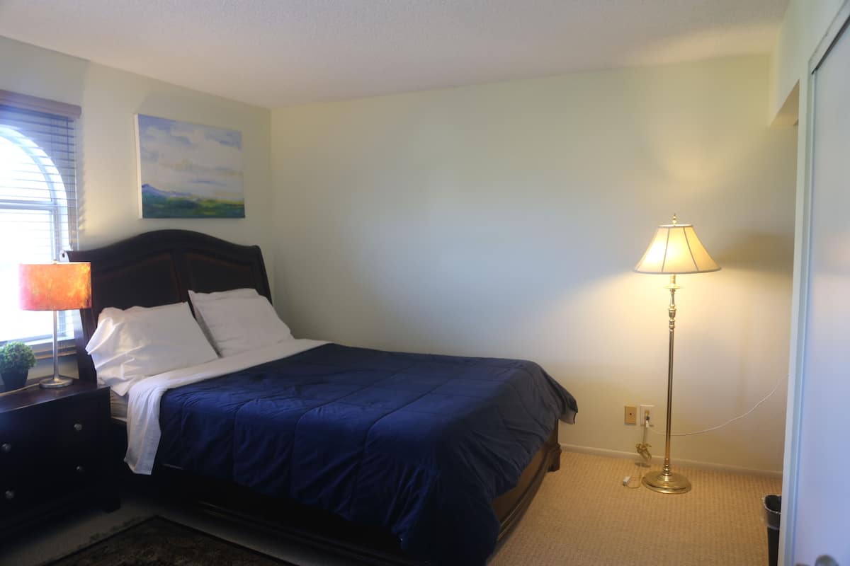 A bedroom with a bed, nightstand, lamp, and a painting on the wall.