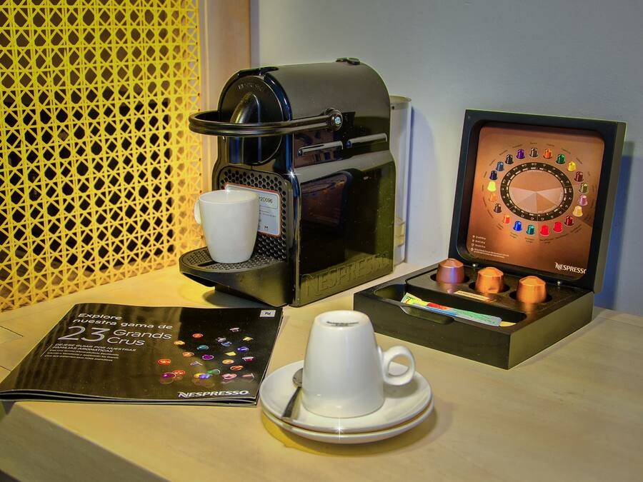Una máquina de café Nespresso con una taza y un plato, un menú y un dispensador de cápsulas de café.