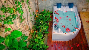 Een hottub met water, omringd door groen en een stenen muur.