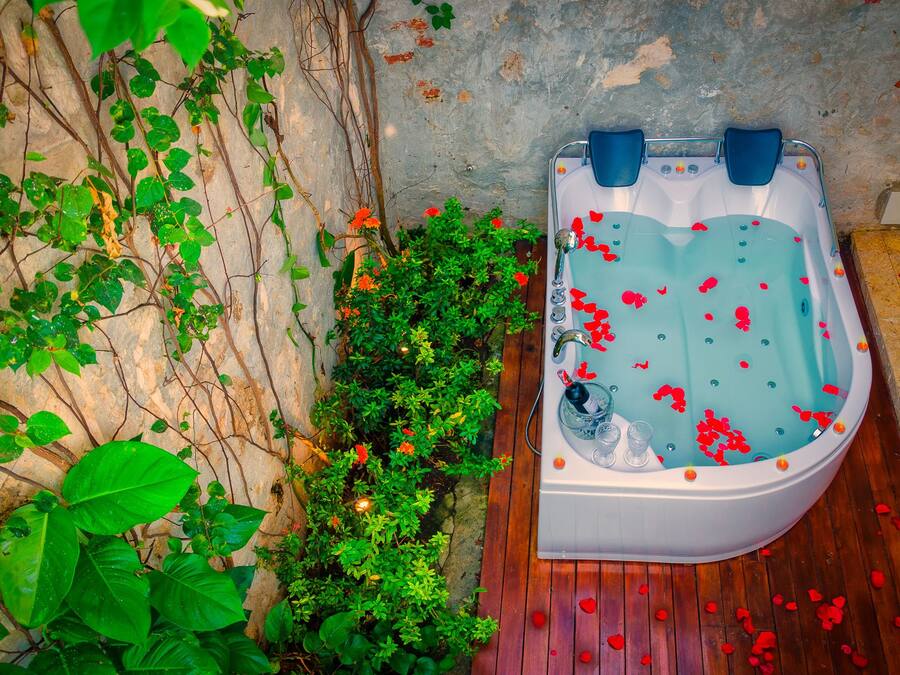 Un jacuzzi con agua, rodeado de follaje y un muro de piedra.