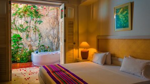 Hotelkamer met een bed, een bedlamp, een groot raam met uitzicht op groen en een bad.
