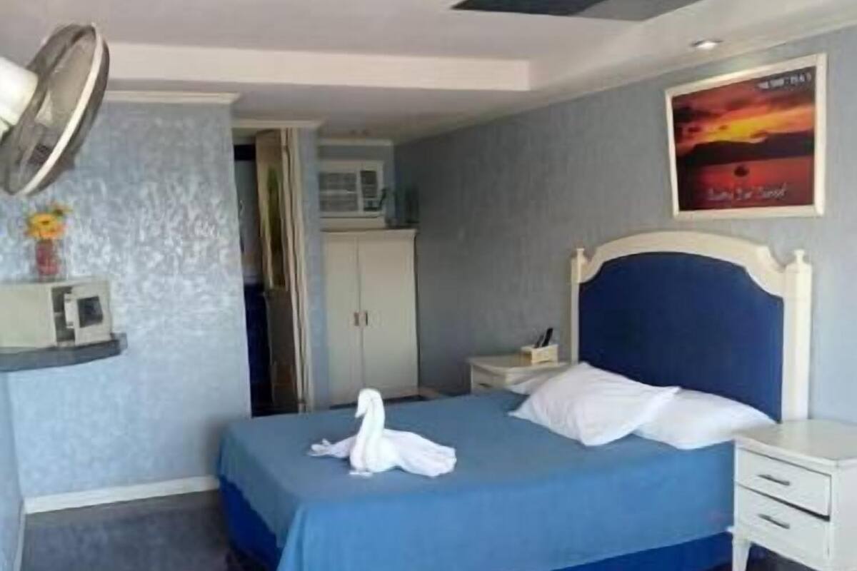 Una habitación de hotel con cama, mesita de noche, televisión montada en la pared y ventilador de techo.