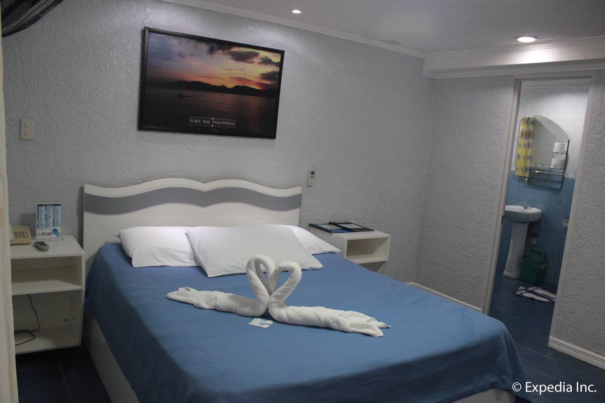 Habitación de hotel con cama, mesita de noche, un cuadro en la pared y un baño visible a través de una puerta abierta.