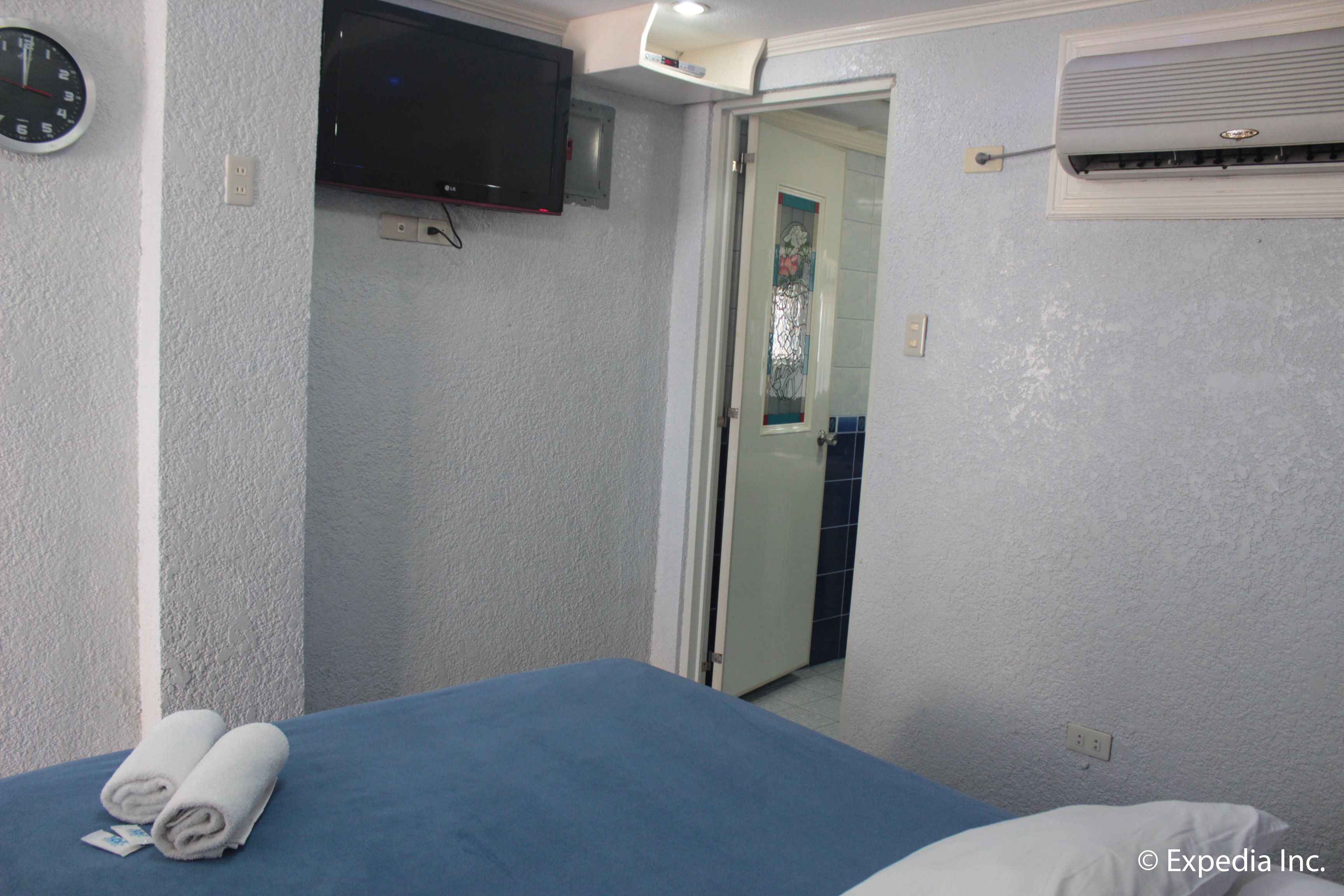 Habitación de hotel con cama, televisor de pantalla plana montado en la pared, equipo de aire acondicionado y puerta que da a otra habitación.