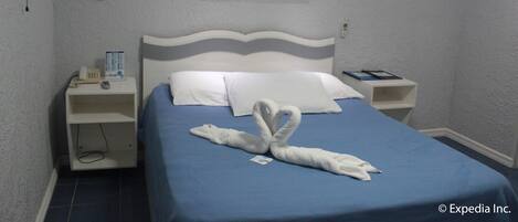 Habitación de hotel con cama, mesita de noche, televisor montado en la pared y un cuadro de un atardecer.