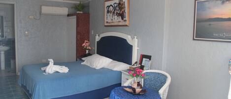 Una habitación de hotel con una cama, una mesita con un florero, una silla y un cuadro colgado en la pared.