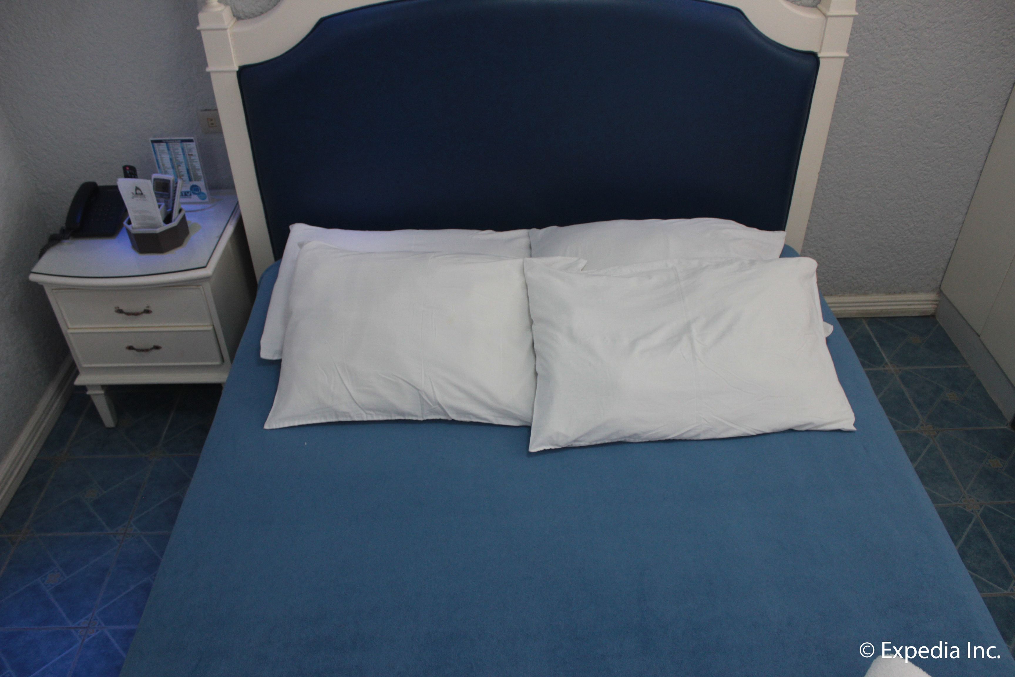 Een keurig opgemaakt bed met witte kussens en een blauwe spreidek in een hotelkamer.