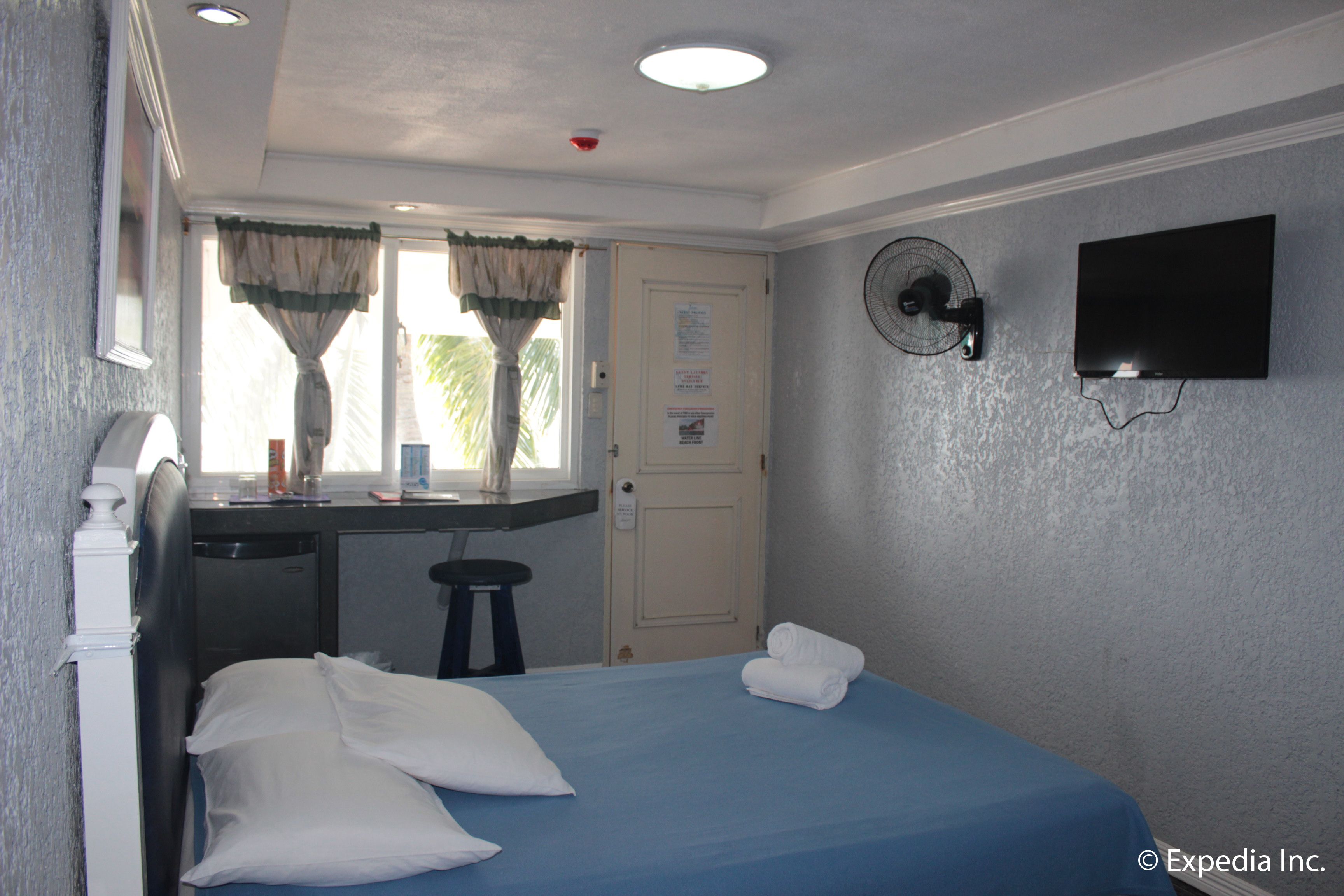A hotel room with a bed, a desk, a chair, a TV, and a window with curtains.