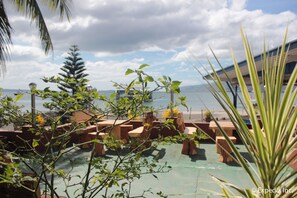 A terrace with wooden seating, a view of the sea, and a palm tree. - Blue Rock Beach Resort (Olongapo)