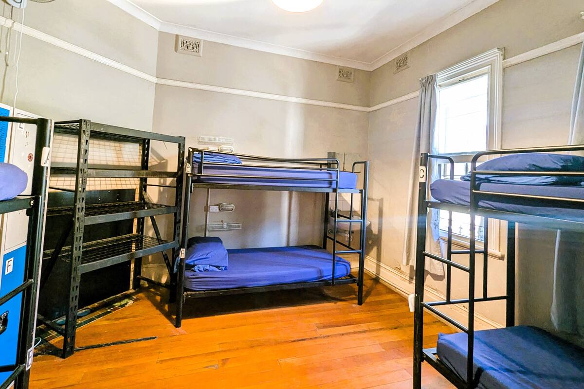 A dormitory room with bunk beds, a desk, and a ceiling fan.