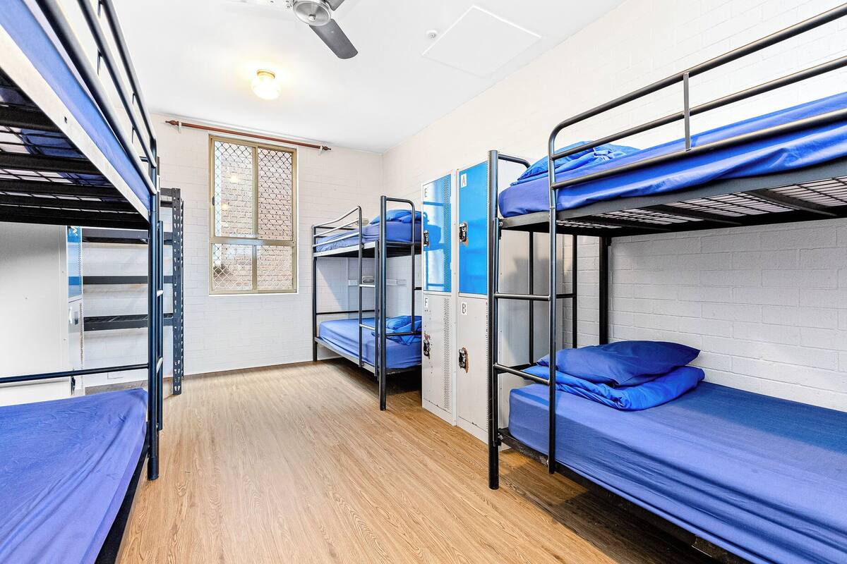 A dormitory room with bunk beds, lockers, and a window with a decorative screen.