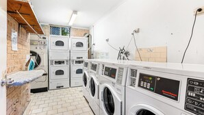 Een wasserette met meerdere wasmachines en drogers, een droogrek en een bakstenen muur.