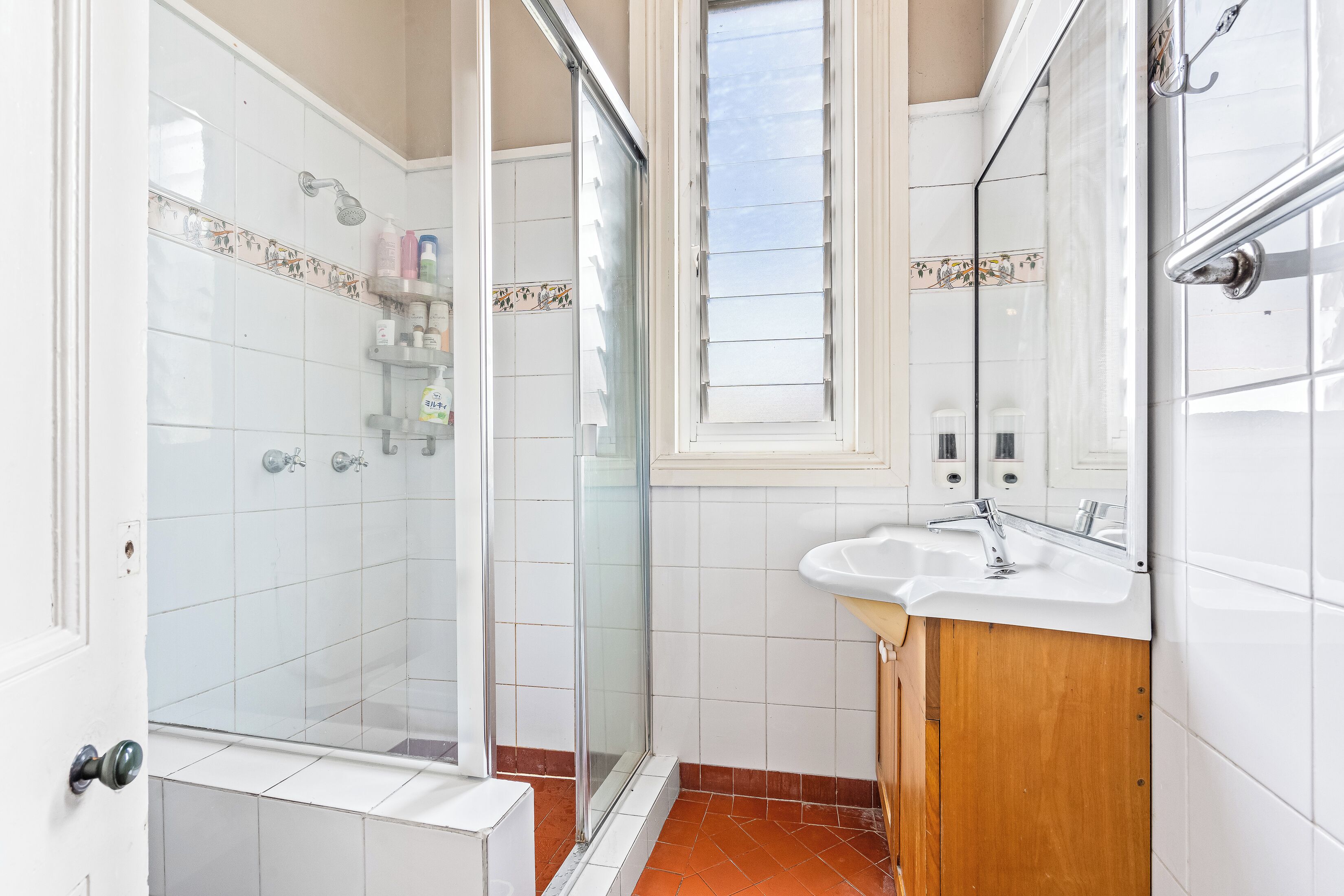 A bathroom with a glass shower enclosure, a white sink, and a wooden cabinet.
