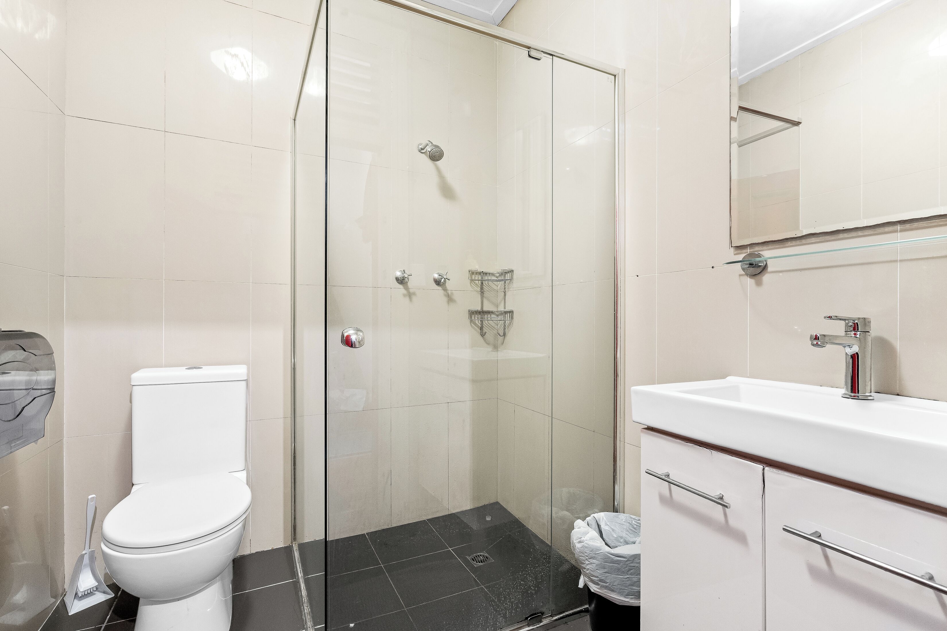 Un baño moderno con ducha envuelta en vidrio, inodoro blanco y lavamanos con espejo superior.
