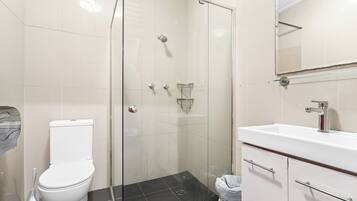 Un baño moderno con ducha envuelta en vidrio, inodoro blanco y lavamanos con espejo superior.