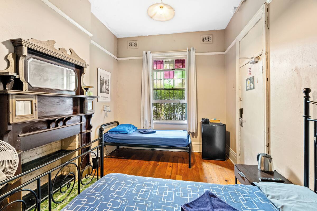 A room with a bed, a wooden dresser, a window with curtains, and a radiator.