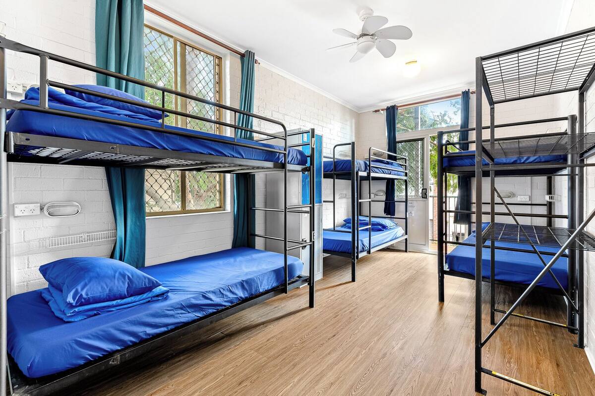 A dormitory room with bunk beds, a ceiling fan, and a window with curtains.