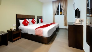 Une chambre d’hôtel avec deux lits, une table de chevet avec un téléphone, une petite armoire, une télévision et une fenêtre avec des rideaux.