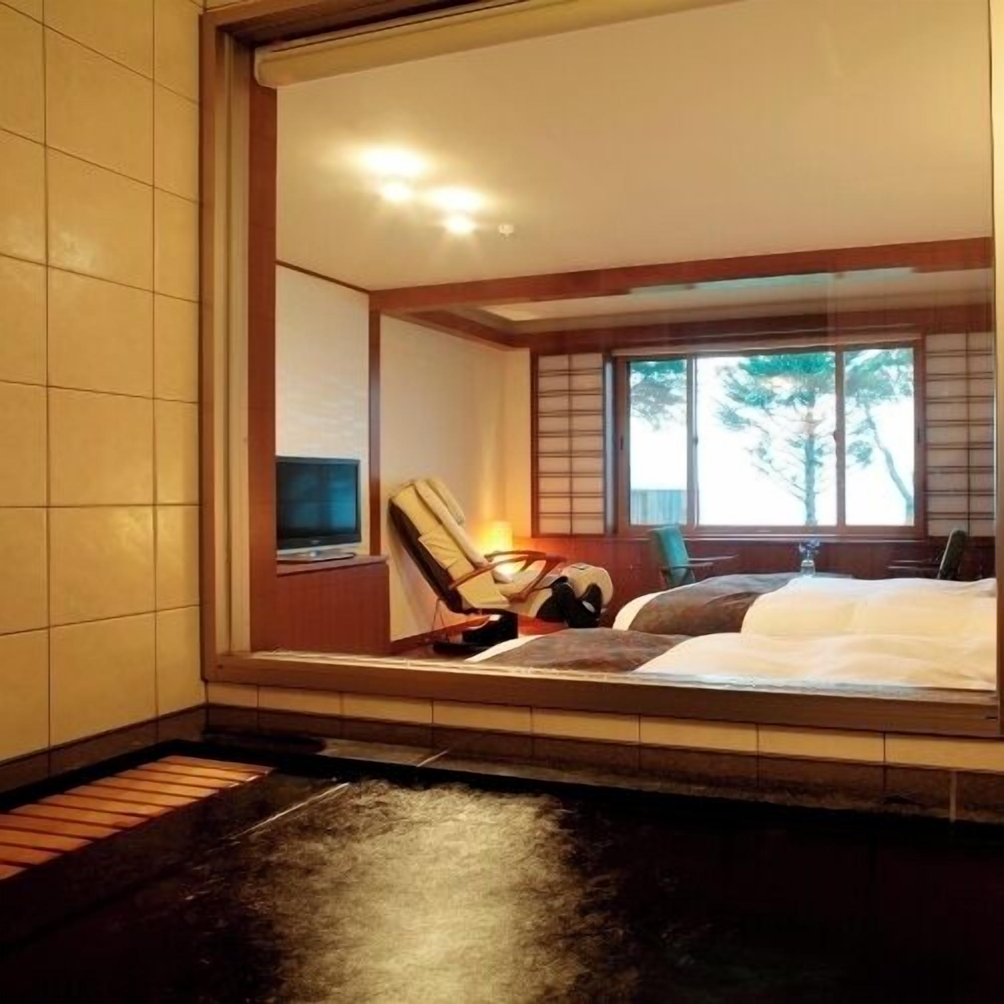 Una habitación con una cama, una silla, un televisor y una ventana que da a árboles.