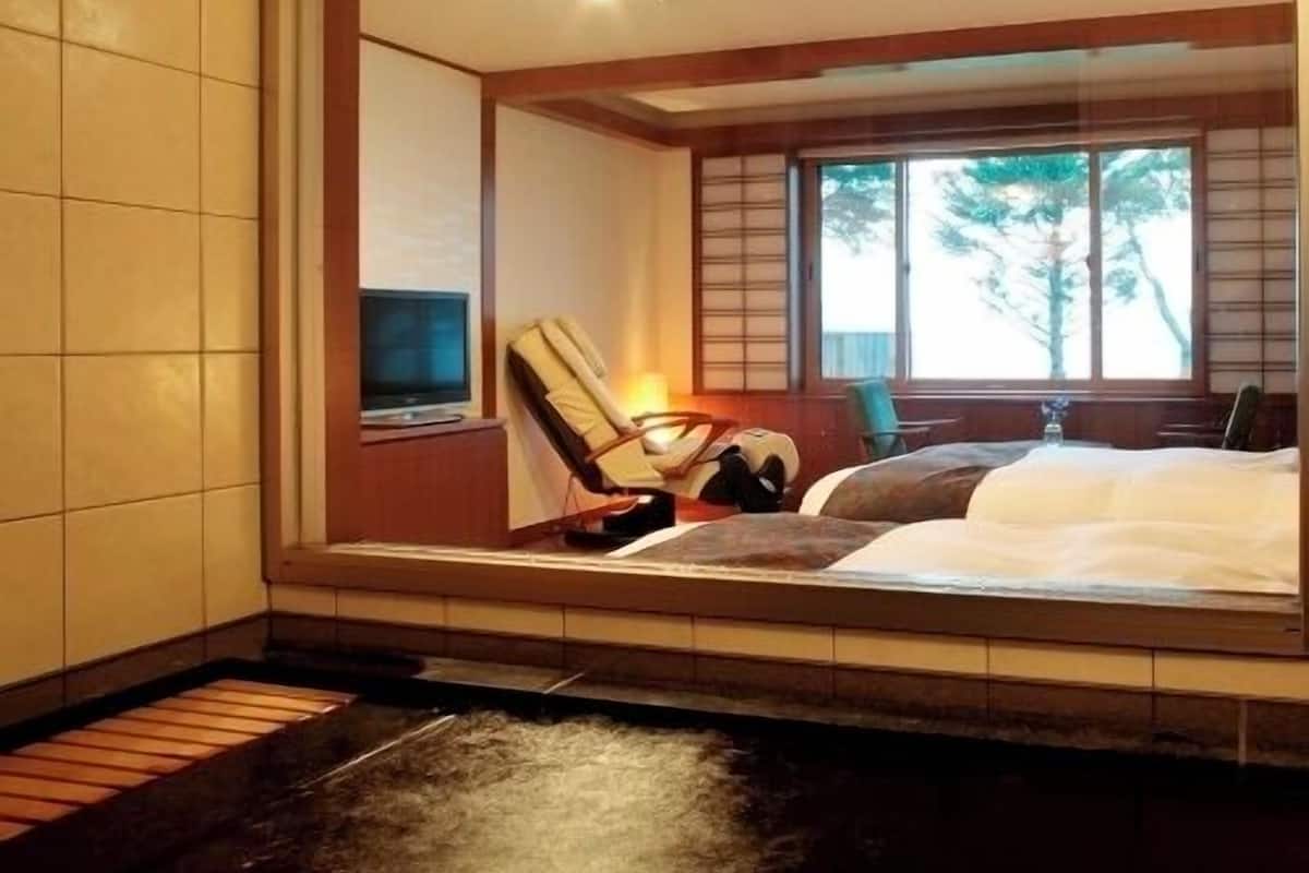 A room with a bed, a chair, a TV, and a window with a view of trees.