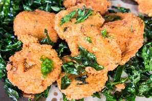 A close-up of breaded and fried food items, possibly chicken cutlets, served on a bed of green leafy vegetables. - OYO 1085 Hotel Budhil Park (Visakhapatnam)