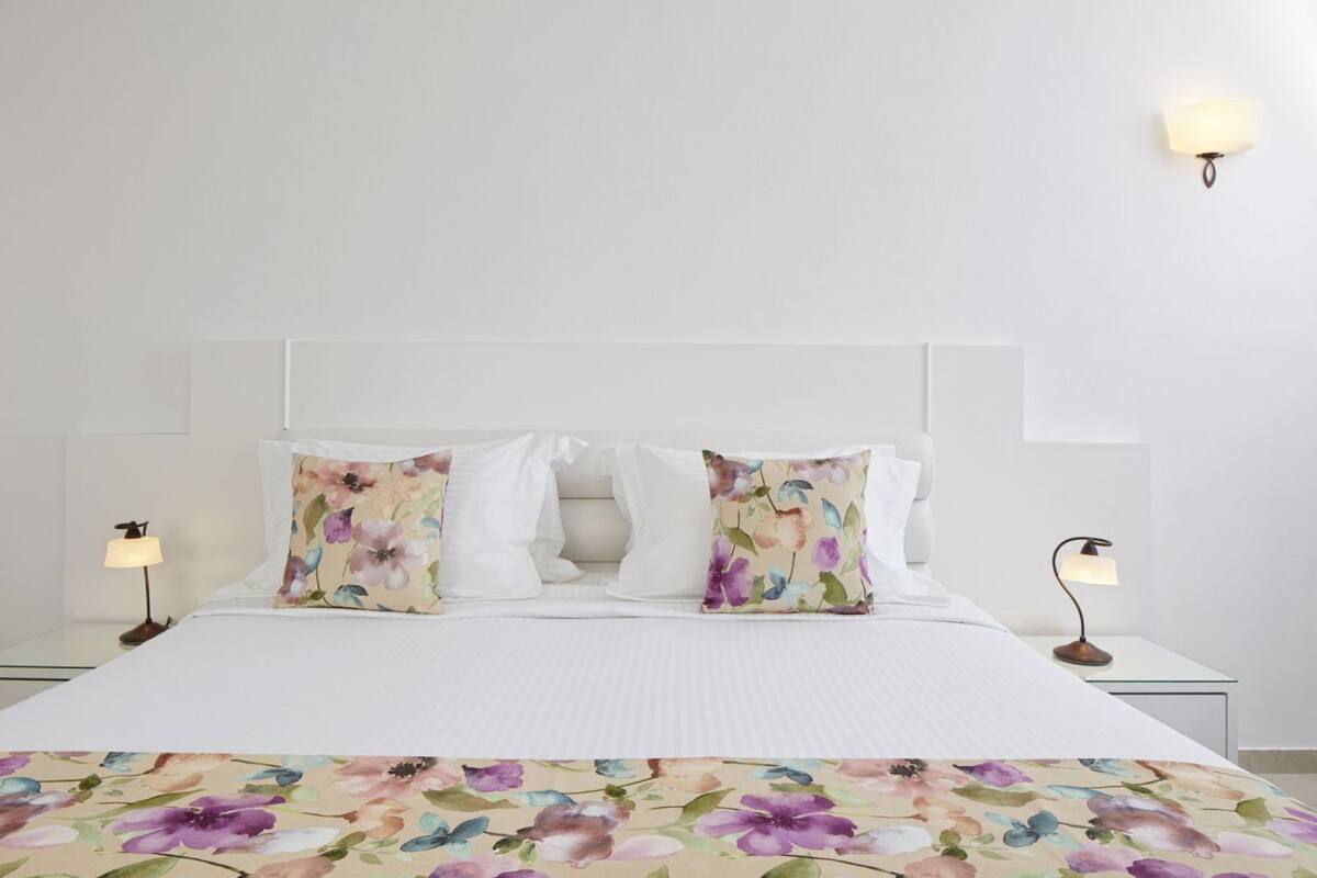 A neatly made bed with white bedding and floral-patterned pillows, flanked by two bedside lamps on white nightstands.