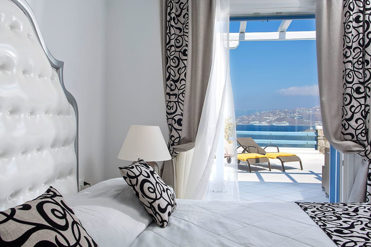A bedroom with a large bed, a bedside lamp, and a view of the sea.